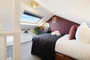 A bedroom with a bed, a skylight, a mirror, and a wall-mounted shelf.