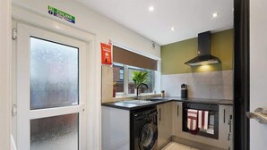 A compact kitchen with a washing machine, a stove, and a microwave. - Modern 4BR with Easy Access to Town and Station (Darlington)