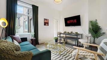 A living room with a sofa, coffee table, TV, and a plant.
