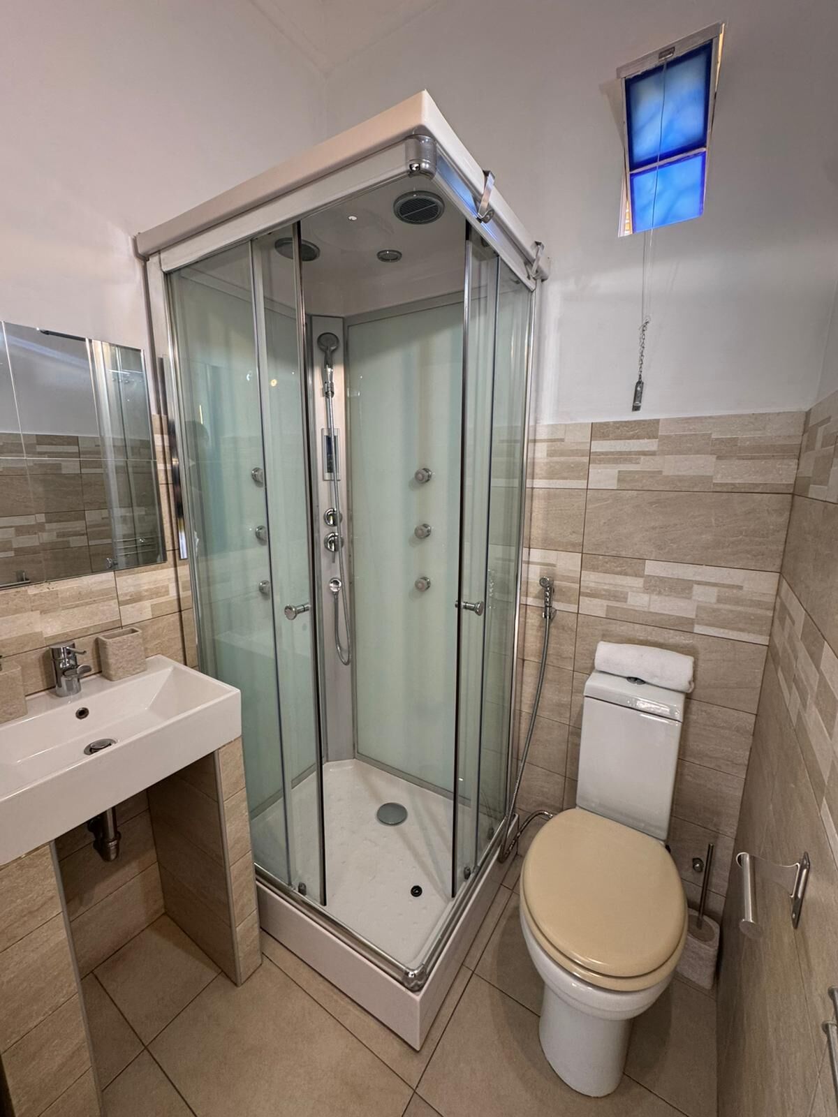 Een moderne badkamer met een douchecabine van glas, een wit wastafeltje en een toilet.