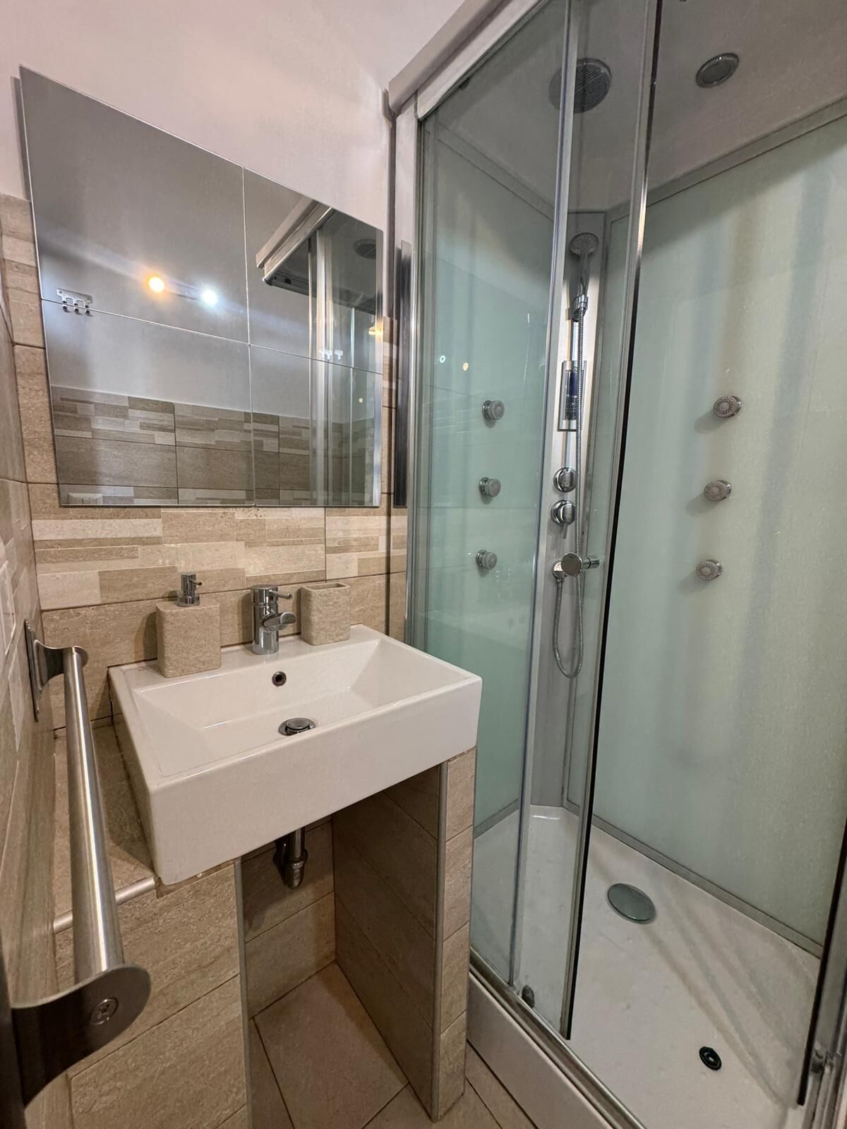 A modern bathroom with a glass shower enclosure, a white sink, and a mirror above it.