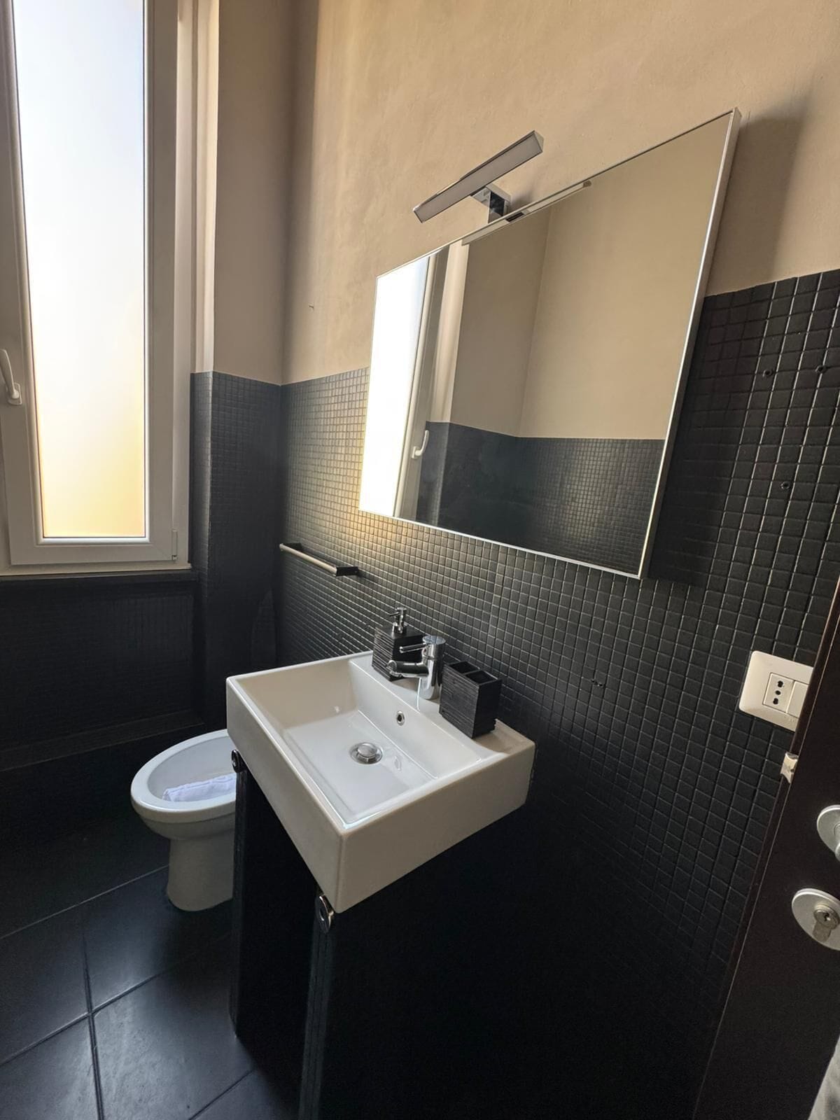 Casa de banho com lavatório branco, espelho e sanita.