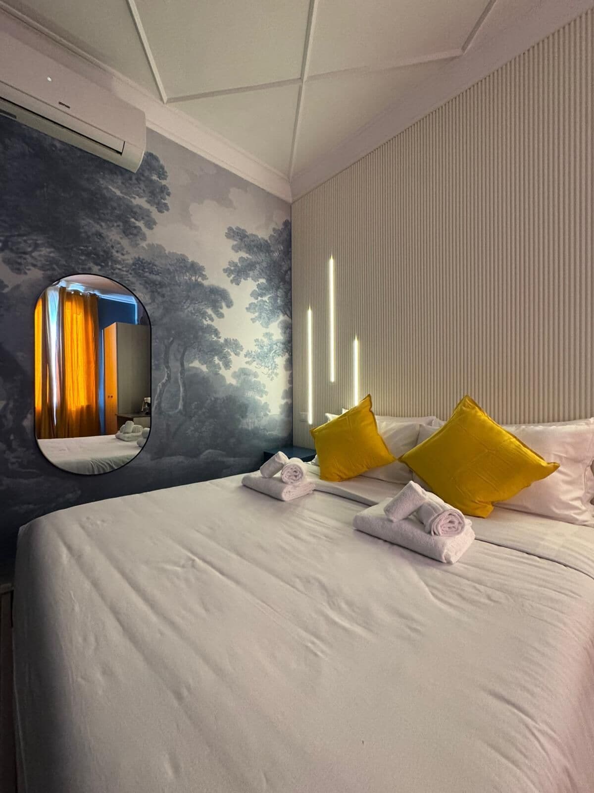 Una habitación de hotel con una cama, un espejo y una pared con líneas verticales.