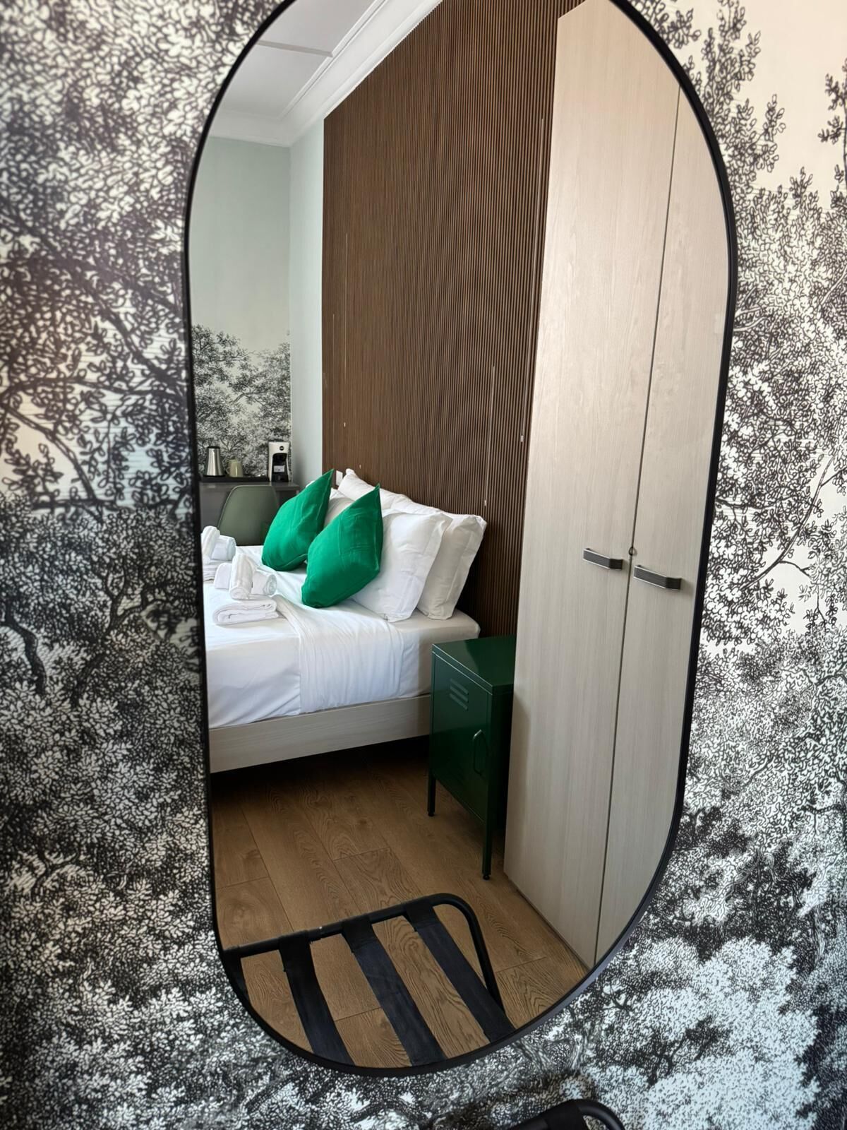 Een slaapkamer met een bed, kussens, een nachtkastje, een garderobe en een spiegel.