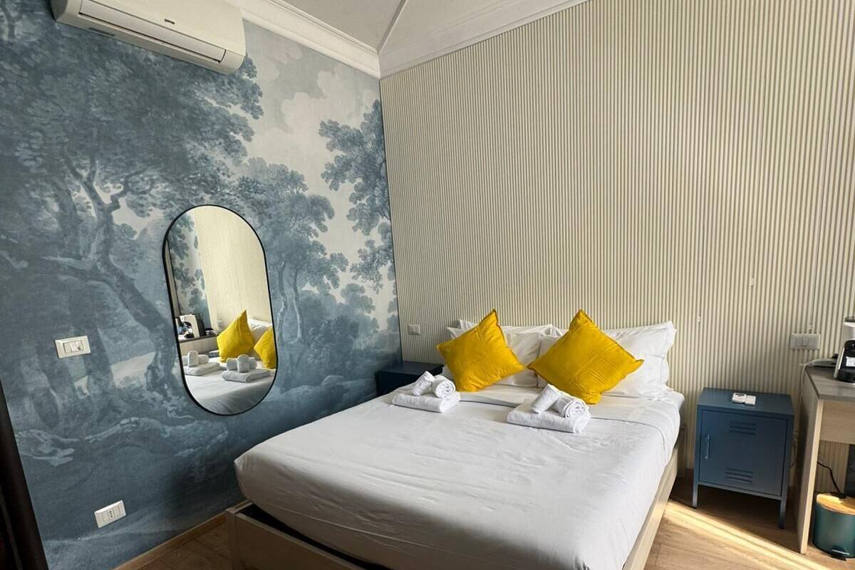 A bedroom with a bed, a mirror, a nightstand, and a wall with vertical lines.