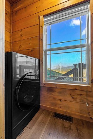 A room with a large window, wooden walls, and a black appliance, possibly a washer or dryer. - LeConte Views - Hot Tub - Game Loft - Remodeled (Gatlinburg)