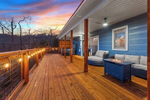 A wooden deck with a railing, a sofa, a table with a fire pit, and a window. - LeConte Views - Hot Tub - Game Loft - Remodeled (Gatlinburg)