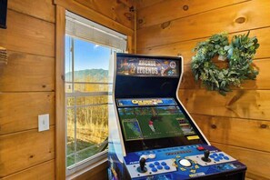 Ein Holzblockhaus-Innenraum mit Spielkonsole, einem Fenster mit Landschaftsblick und einem Kranz an der Wand.