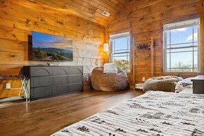 A wooden cabin bedroom with a bed, a dresser, a television, and a large window. - LeConte Views - Hot Tub - Game Loft - Remodeled (Gatlinburg)