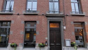 A brick building with multiple windows, a central door, and small planters on the ground floor. - La Petite Histoire (Ath)