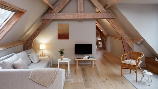 A loft bedroom with exposed wooden beams, a bed, a TV, a small table, and a chair. - La Petite Histoire (Ath)