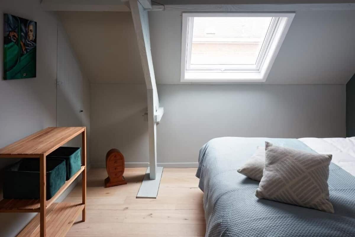 A bedroom with a skylight, a wooden desk, and a bed with pillows.