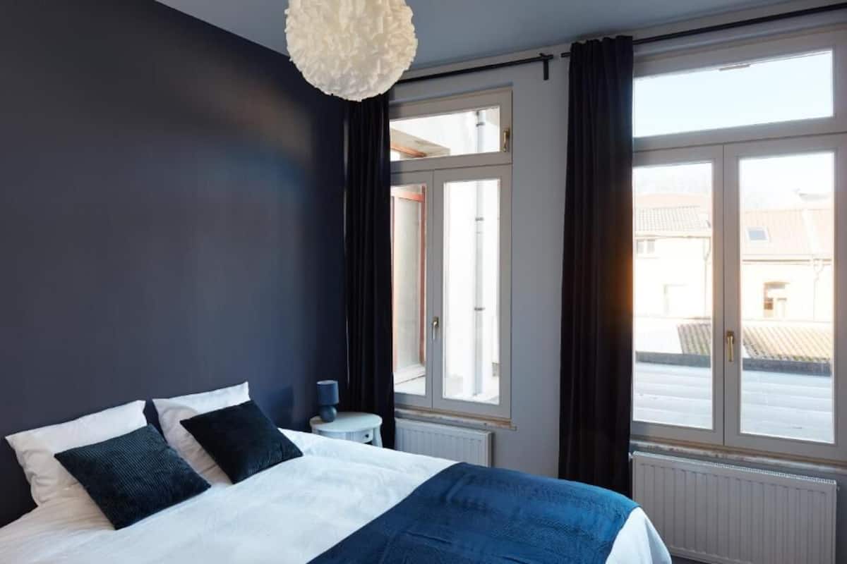 A bedroom with a bed, a nightstand, a lamp, and a window with curtains.