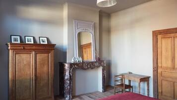 A bedroom with a bed, a wooden wardrobe, a small table, a mirror, and a fireplace.