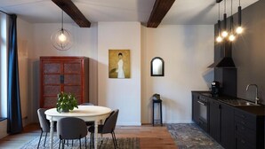 A modern kitchen with dark cabinetry, a round dining table, and a hanging light fixture. - La Petite Histoire (Ath)
