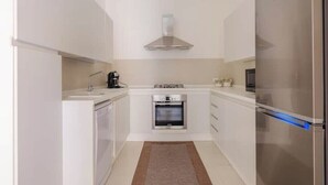 A compact kitchen with white cabinetry, a built-in oven, a stainless steel range hood, and a refrigerator. - Cozy apartment in Lecce, parking (Lecce)