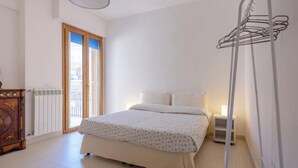 A bedroom with a bed, a radiator, a wooden cabinet, a hanging clothes rack, and a door leading to a balcony. - Cozy apartment in Lecce, parking (Lecce)