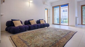 A living room with a large rug, two sofas, a wall-mounted light, and a sliding glass door to the outside. - Cozy apartment in Lecce, parking (Lecce)