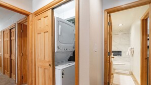 Een wasserette met een wasmachine en droger, houten deuren, en een badkamer met douche en bad.
