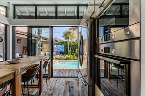 Une cuisine moderne dotée d’un four encastré de marque Bosch, d’une table à manger en bois avec des chaises, et offrant une vue sur une piscine.