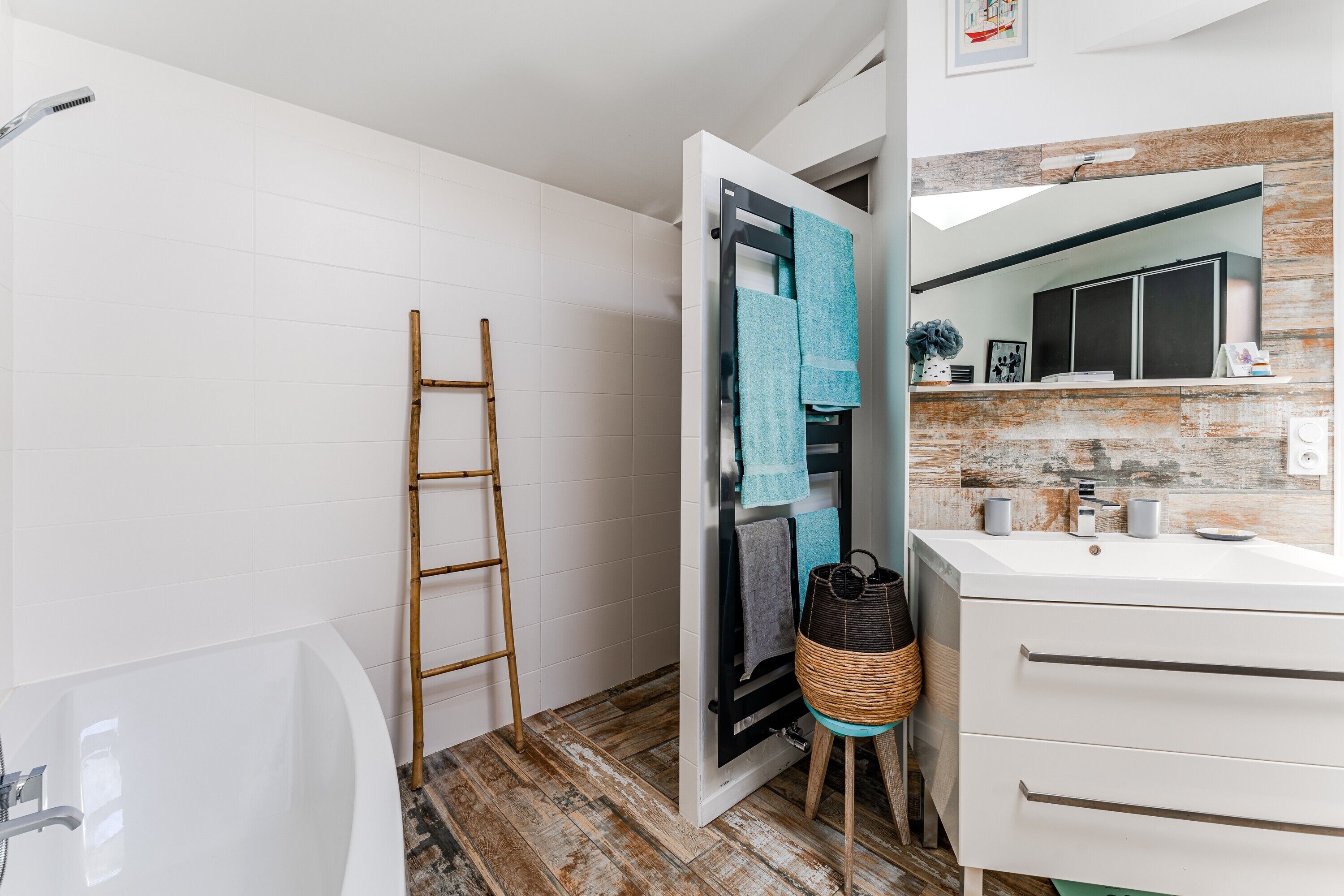 A bathroom with a bathtub, a towel rack with towels, a wicker basket, and a mirror with a wooden backsplash.