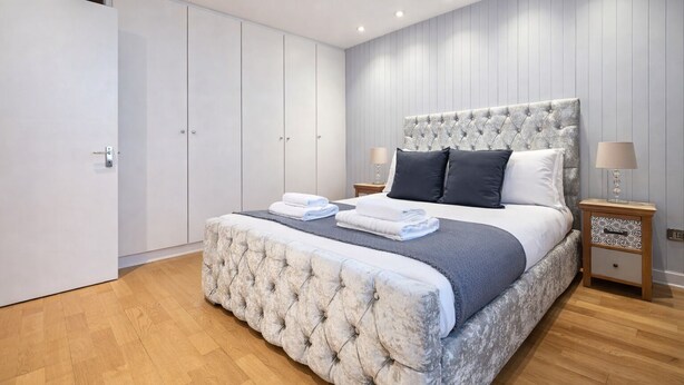 A bedroom with a large bed, a wardrobe, and a nightstand with a lamp. - Central London Stay | Steps from Regent’s Park (London)