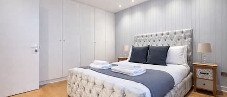 A bedroom with a large bed, a wardrobe, and a nightstand with a lamp.