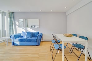 A modern living room with a blue sofa, a white dining table, and blue chairs. - Central London Stay | Steps from Regent’s Park (London)