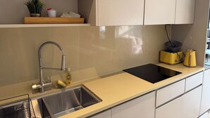 A modern kitchen with a stainless steel sink, a built-in stove, and a shelf above the sink. - London 2 Bed Premium Flat (London)