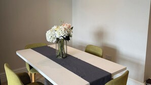 A dining area with a rectangular table, four chairs, and a vase with flowers. - London 2 Bed Premium Flat (London)