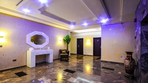 A lobby with a reception desk, a mirror, a plant, and a vase. - KELVIC SUITES (Owerri)
