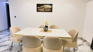 A modern dining area with a white table, beige chairs, a vase with flowers, and a framed picture on the wall. - KELVIC SUITES (Owerri)