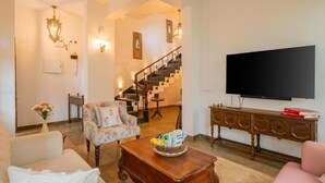 A living room with a sofa, a chair, a coffee table, a TV, a staircase, and a wall-mounted TV. - ELIVAAS Amayah Vayu 6 BHK Villa (Assagao)
