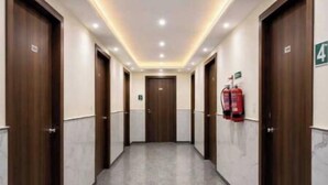 A hotel corridor with wooden doors, a fire extinguisher, and a number sign on the wall. - Hotel Luxe Stay - Delhi Airport (New Delhi)