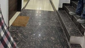 A hallway with a marble floor, a wooden door at the end, and a person standing on the stairs. - Hotel Luxe Stay - Delhi Airport (New Delhi)