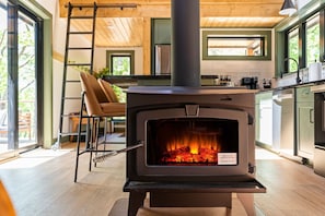 A modern kitchen with a wood-burning stove, a ladder, and a view of the outdoors. - Secluded Cabin with King Bed and Fire Pit on 48 Private Acres (Carroll County)