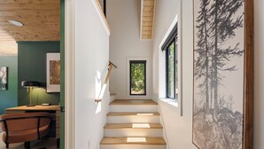 A staircase leading to a second floor with wooden steps, a desk with a chair, and framed artwork on the walls. - Secluded Cabin with King Bed and Fire Pit on 48 Private Acres (Carroll County)
