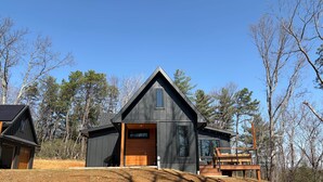 A modern cabin with a sloped roof, a large deck, and a dirt driveway. - Secluded Cabin with King Bed and Fire Pit on 48 Private Acres (Carroll County)