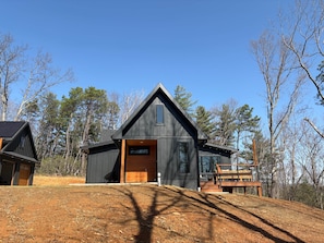 A modern cabin with a sloped roof, a large deck, and a dirt driveway. - Secluded Cabin with King Bed and Fire Pit on 48 Private Acres (Carroll County)