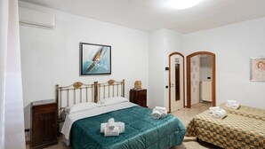 Une chambre d’hôtel avec un lit, une petite table de chevet, une armoire, un tableau au mur et une porte donnant sur une autre pièce.
