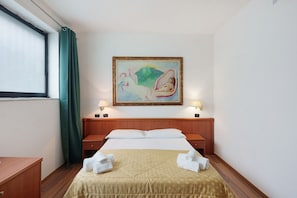 Ein Hotelzimmer mit Bett, zwei Nachttischen, einem Bild an der Wand und einem Fenster mit Vorhängen.