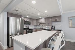 A modern kitchen with stainless steel appliances, a marble backsplash, and a central island with bar stools.
