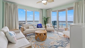 A spacious living room with a balcony, a ceiling fan, and a view of the ocean. - Pelican Perch! 3BR 3BA Corner Beachfront Condo w/ Epic Views, Sleeps 10 (Panama City Beach)
