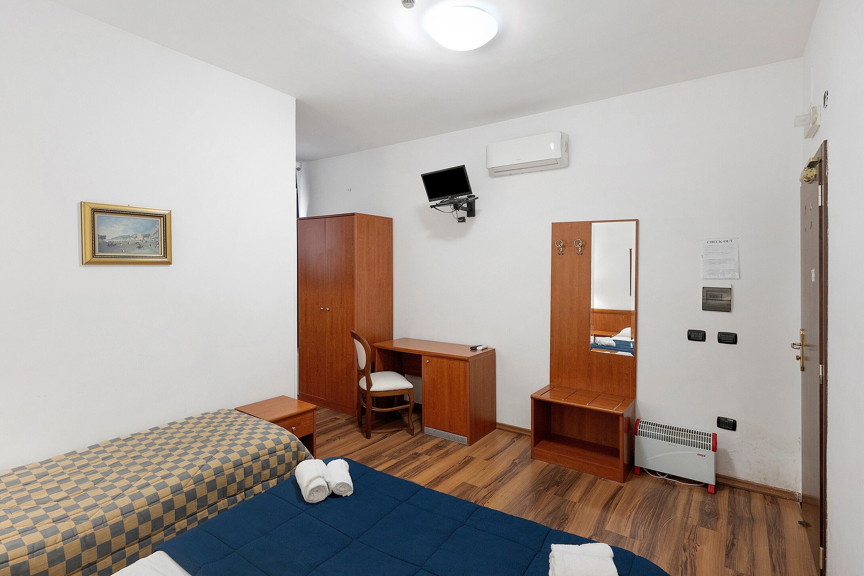 Une chambre à coucher comprenant un lit, un bureau, une chaise, une armoire, un radiateur et un téléviseur.