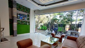 A modern lobby with a glass partition, brown leather sofas, a glass coffee table, and a green wall with a digital display. - Hotel Kalra (Amritsar)