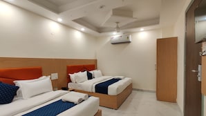 A hotel room with two beds, a wooden headboard, a ceiling fan, an air conditioning unit, and a wardrobe. - Hotel Kalra (Amritsar)