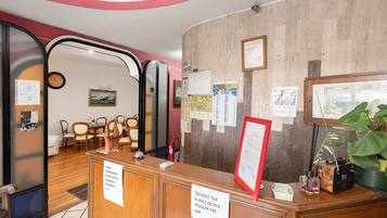 Un espace d’accueil d’hôtel avec un comptoir en bois, des chaises, une horloge et divers panneaux d’affichage.