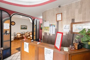 A hotel reception area with a wooden desk, chairs, a clock, and various notices. - H Pompeii Ruiins Apartment Hotel - Standard Quadruple Room 10 (Pompei)