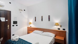 A hotel room with a bed, two bedside tables, a wooden headboard, a blue bedspread, and two wall-mounted lamps. - H Pompeii Ruiins Apartment Hotel - Standard Quadruple Room 10 (Pompei)