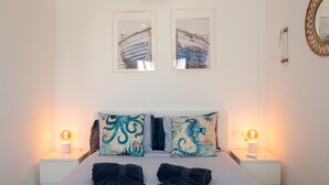 Una cama con dos almohadas, una mesita de noche con lámpara y un espejo instalado en la pared.